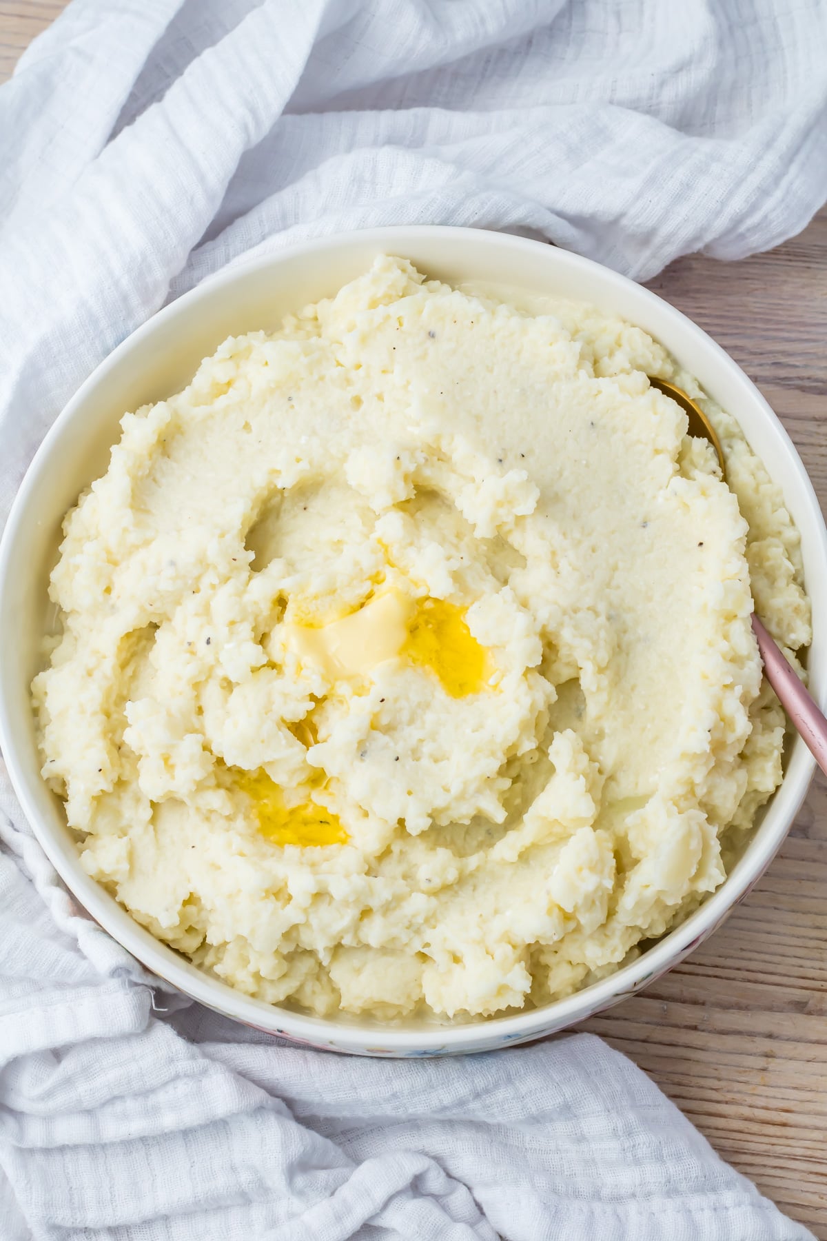 A bowl of cauliflower mash with a pat of melted butter in the center, placed on a light-colored cloth.