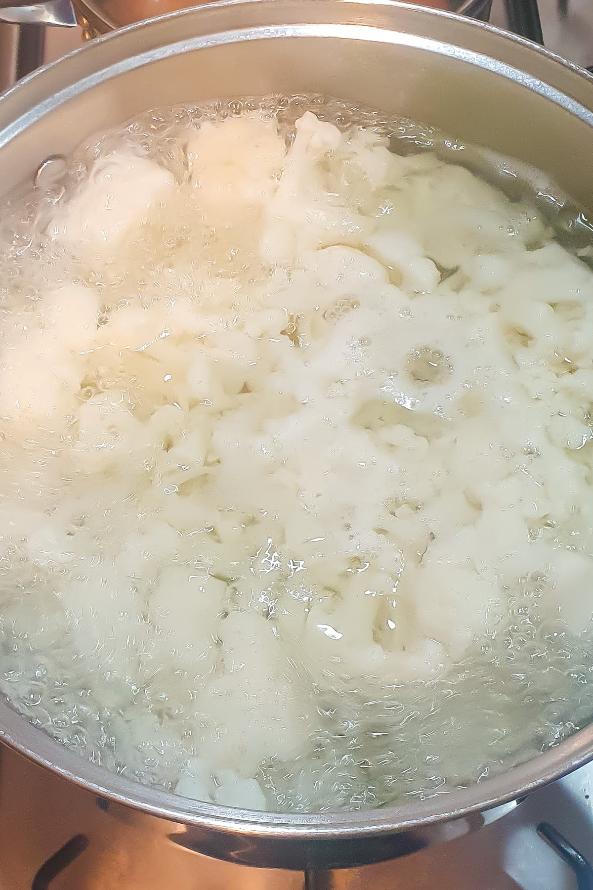 A pot of water boiling with pieces of cauliflower cooking inside on a stovetop.