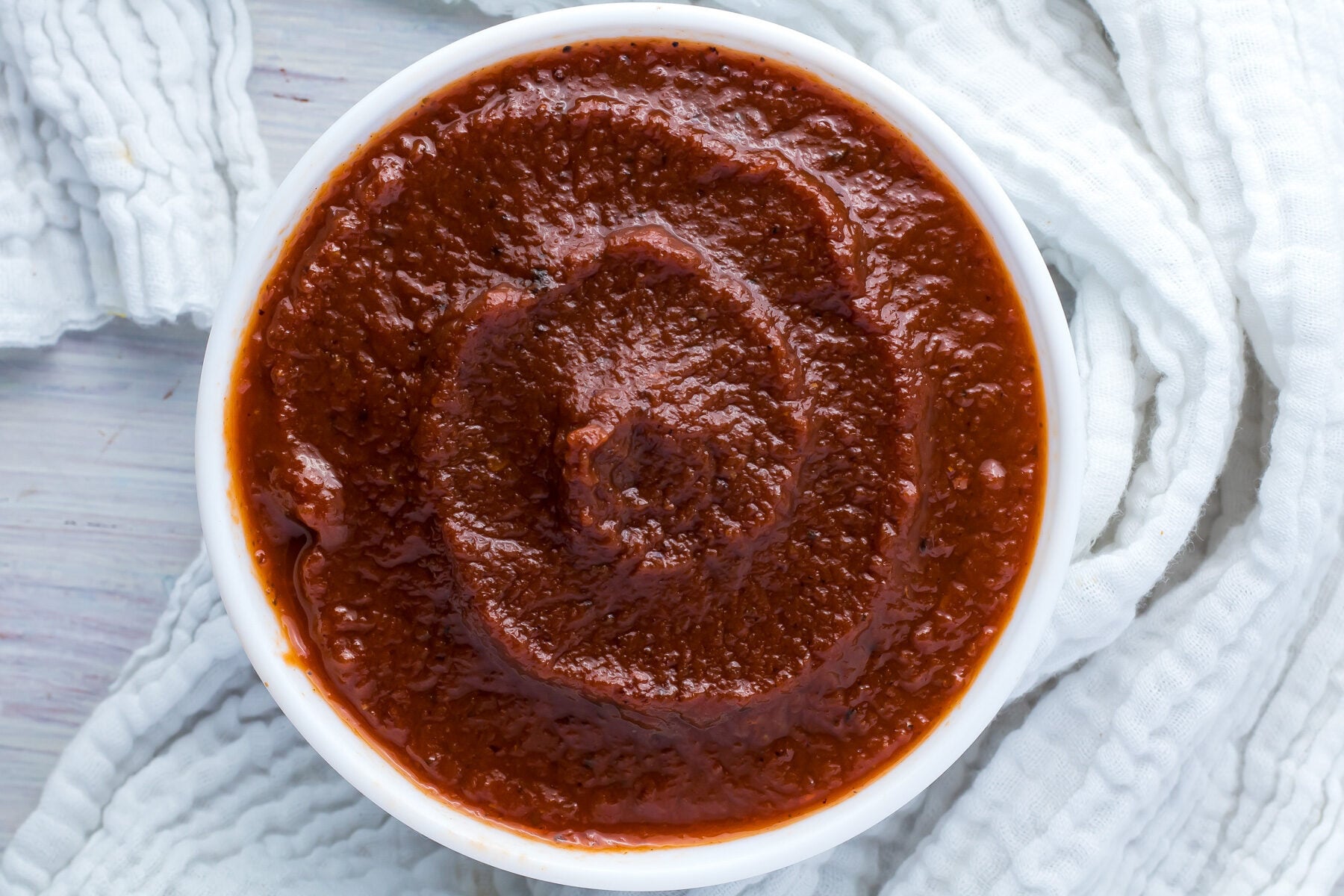 Overhead shot of sugar free bbq sauce in a white bowl surrounded by a white cloth.