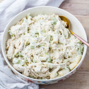 A bowl of Greek yogurt chicken salad mixed with diced celery and a creamy dressing, with a gold spoon resting inside the bowl.