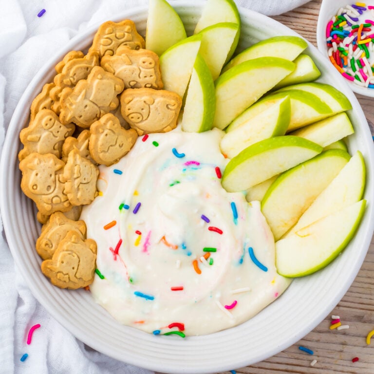 A white bowl with green apple slices, animal-shaped cookies, and healthy dunkaroo dip topped with colorful sprinkles.