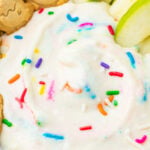 A close-up of healthy dunkaroo dip with colorful sprinkles, surrounded by green apple slices and animal-shaped cookies.