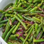 A bowl of cooked honey mustard green beans mixed with sliced red onions and a grainy mustard dressing.