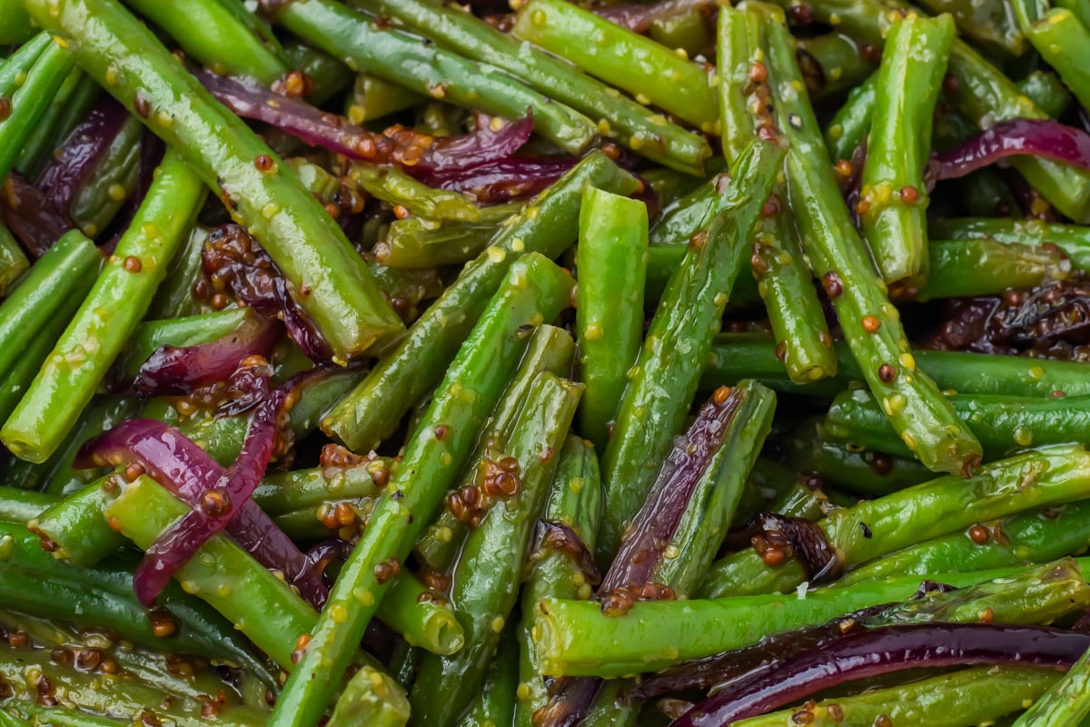 Close-up of cooked honey mustard green beans mixed with sliced red onions and whole grain mustard seeds.