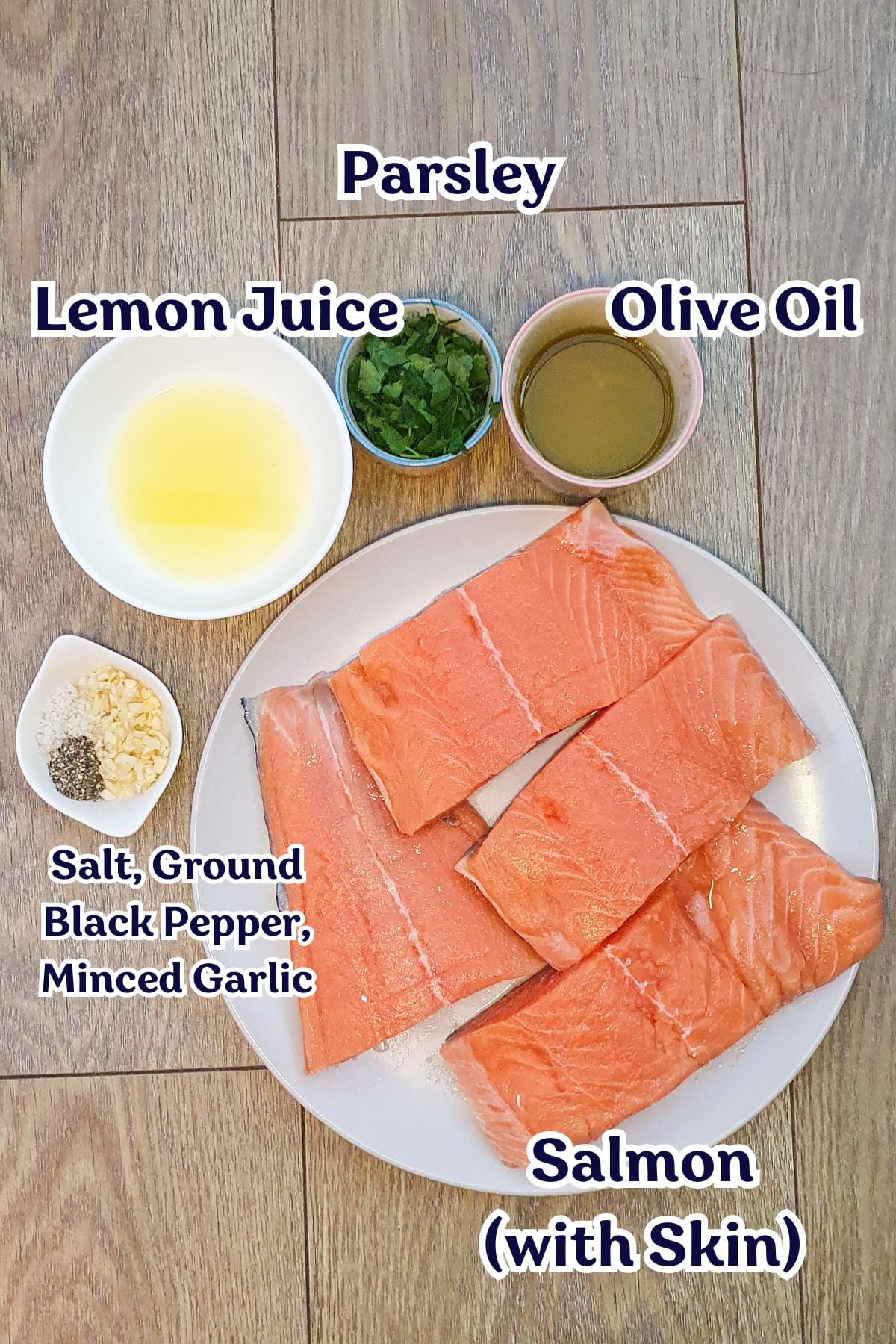 Four raw salmon fillets on a plate with small bowls of parsley, olive oil, lemon juice, minced garlic, salt, and ground black pepper arranged on a wooden surface.