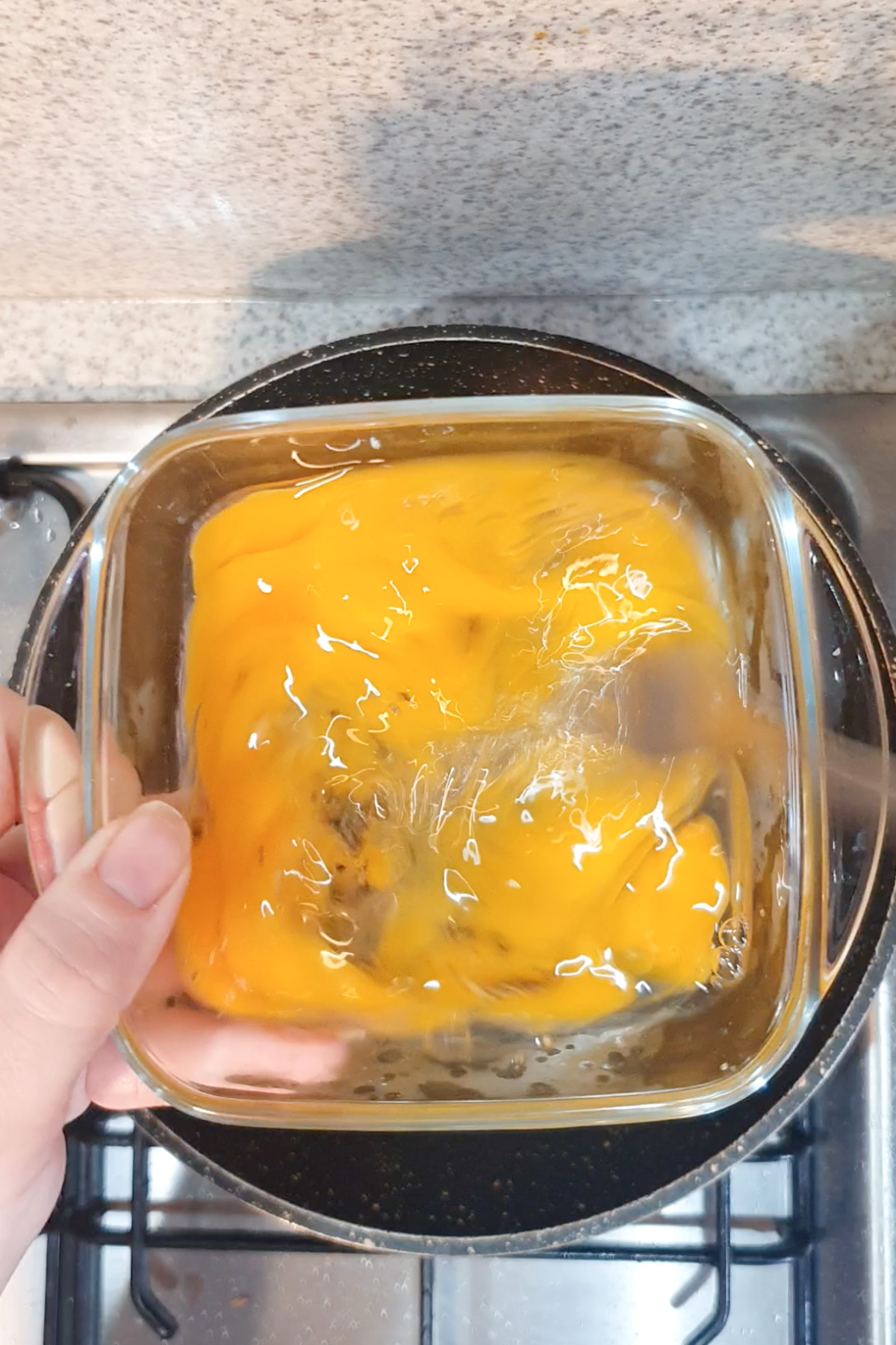 A hand holding a glass bowl with raw beaten eggs above a stove, ready for cooking.