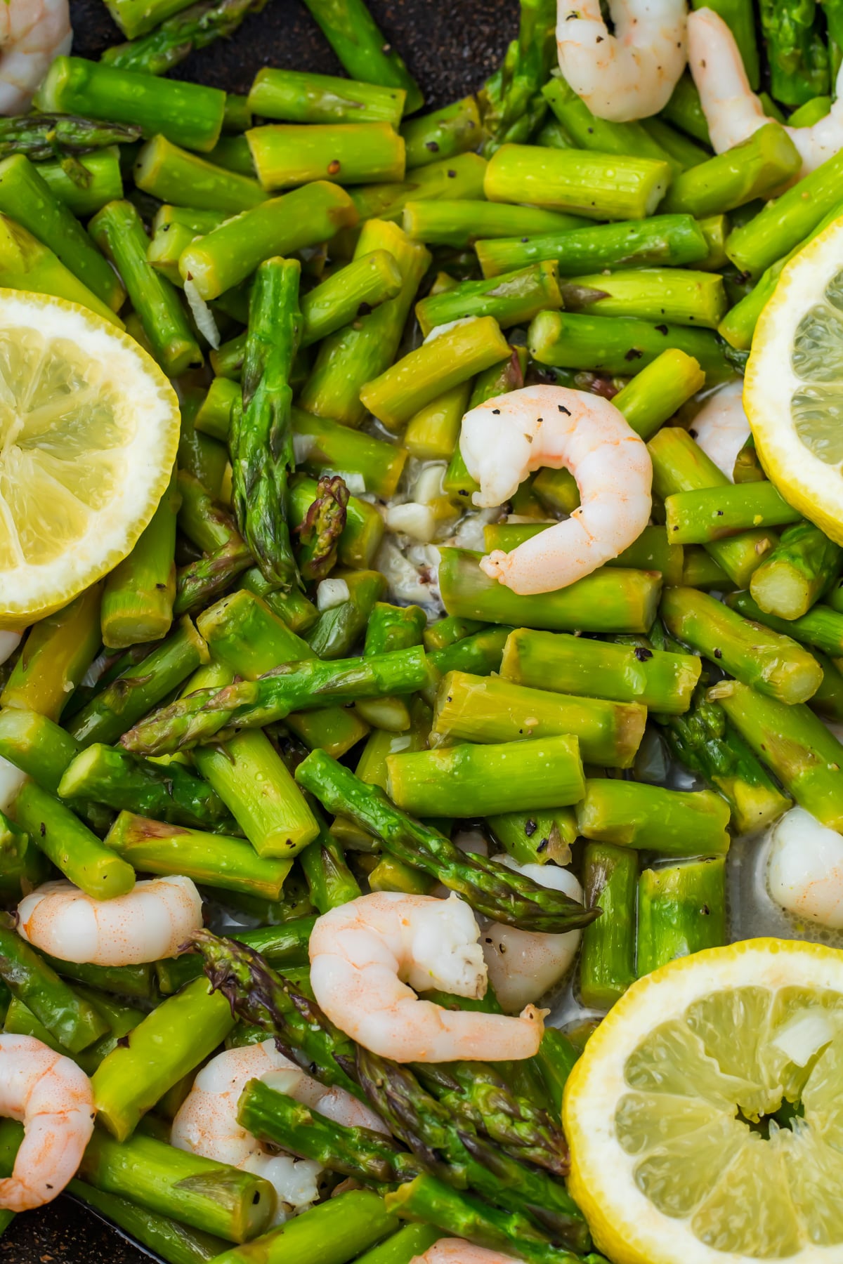 Close-up of cooked shrimp and asparagus, and lemon slices mixed together.