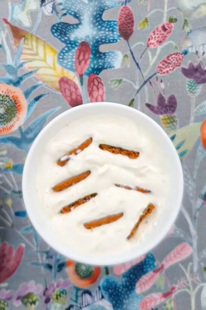 A white bowl with 3 ingredient yogurt cheesecake, and several cookies stuck inside, placed on a colorful floral-patterned surface.