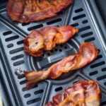 Four cooked strips of bacon sit on the tray inside an air fryer basket.