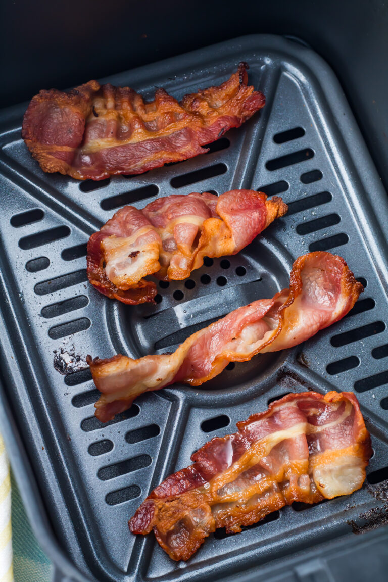 Four cooked strips of bacon sit on the tray inside an air fryer basket.