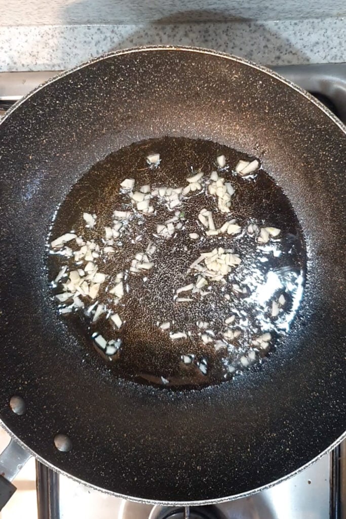 Chopped garlic frying in oil in a nonstick pan on a stovetop, creating the perfect base for sautéing shrimp and asparagus.