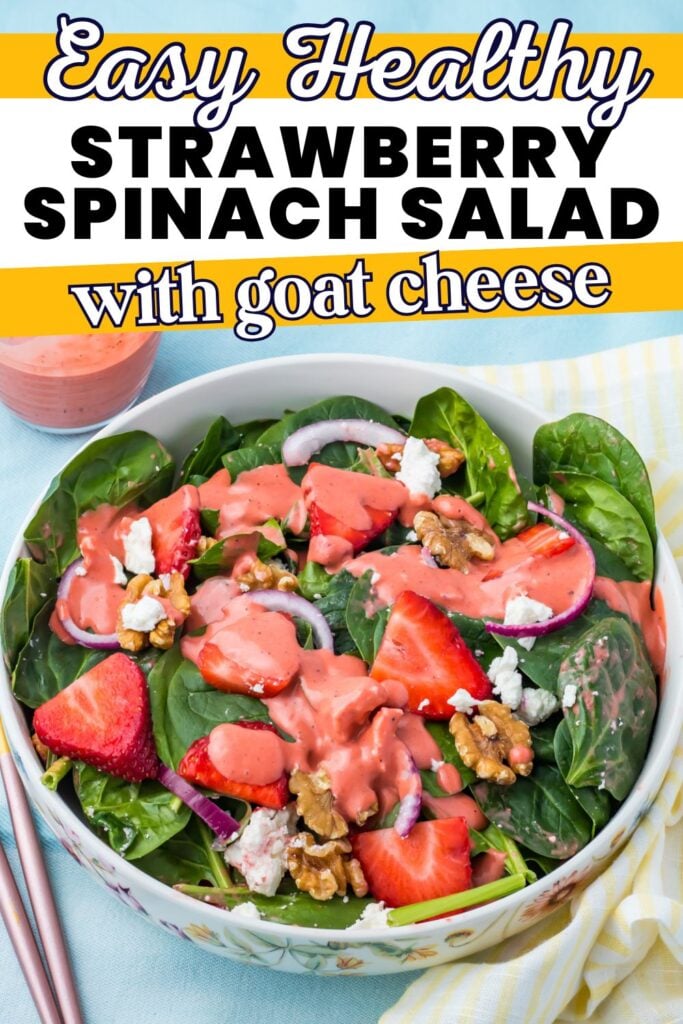 A bowl of strawberry goat cheese salad with spinach, walnuts, red onion, and pink dressing, plus a small bowl of extra dressing nearby. Text overlay reads "Easy Healthy Strawberry Spinach Salad with goat cheese.