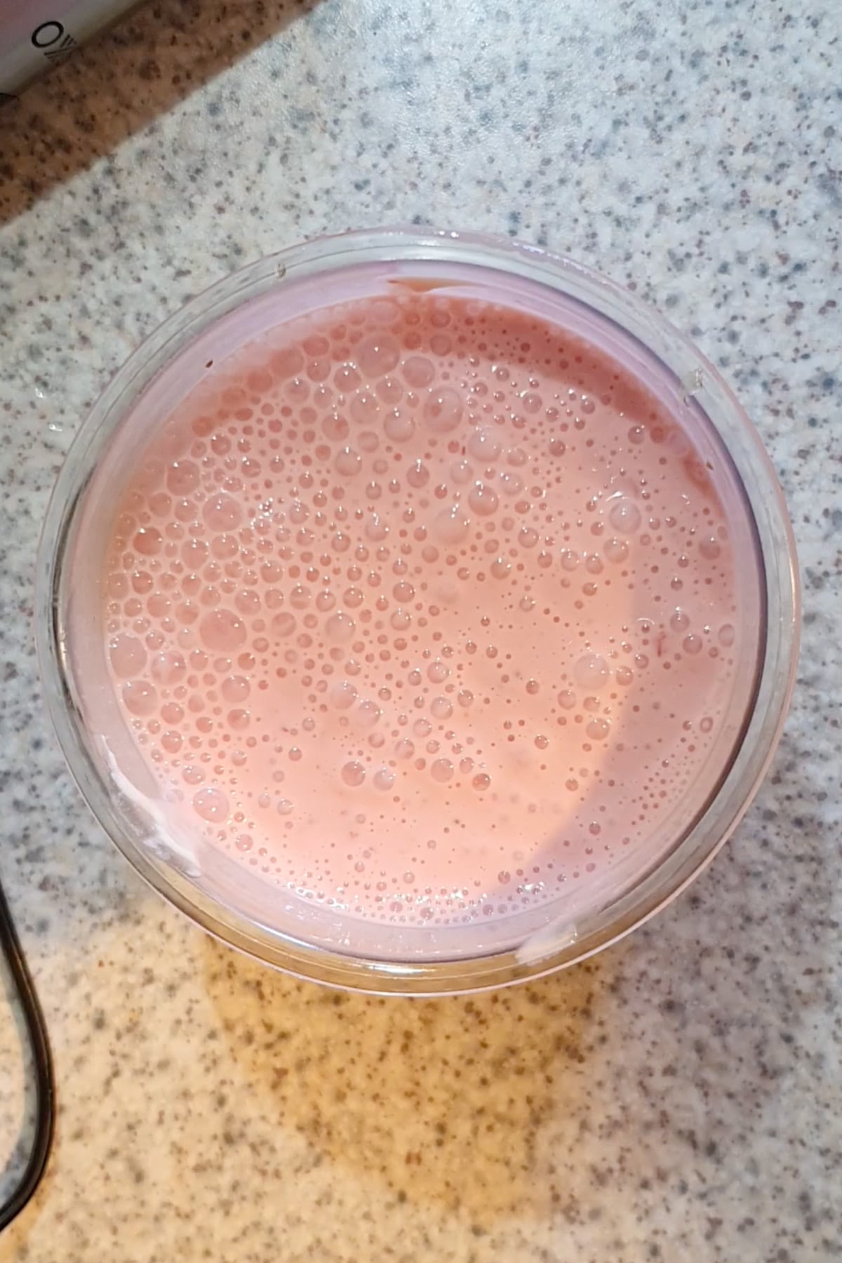 A glass filled with pink, frothy liquid sits on a speckled countertop.