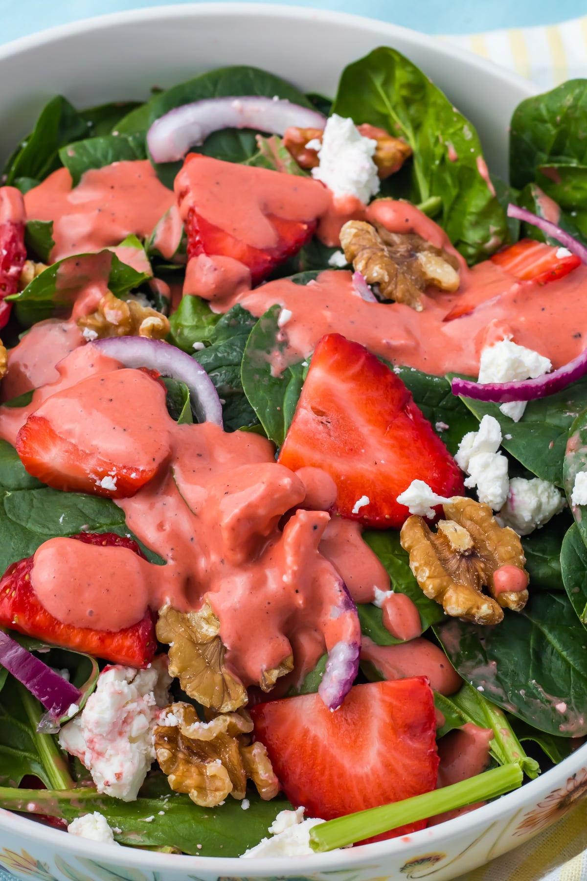 A strawberry salad with goat cheese, with spinach, sliced strawberries, walnuts, red onion, goat cheese, and pink dressing in a white bowl.