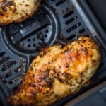 Cooked, seasoned chicken breasts resting in a ninja air fryer basket with visible grill marks and a slightly browned surface.