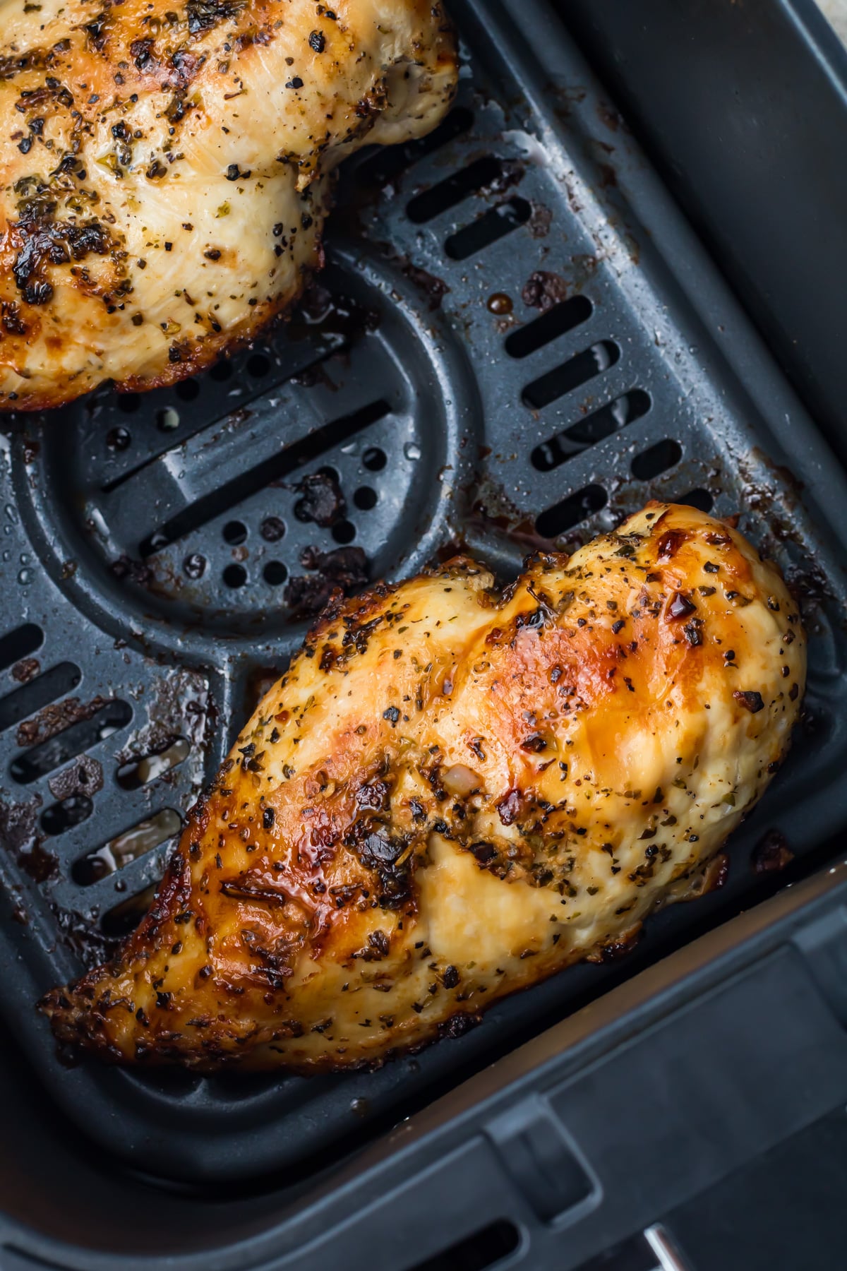 Cooked, seasoned chicken breasts resting in a ninja air fryer basket with visible grill marks and a slightly browned surface.