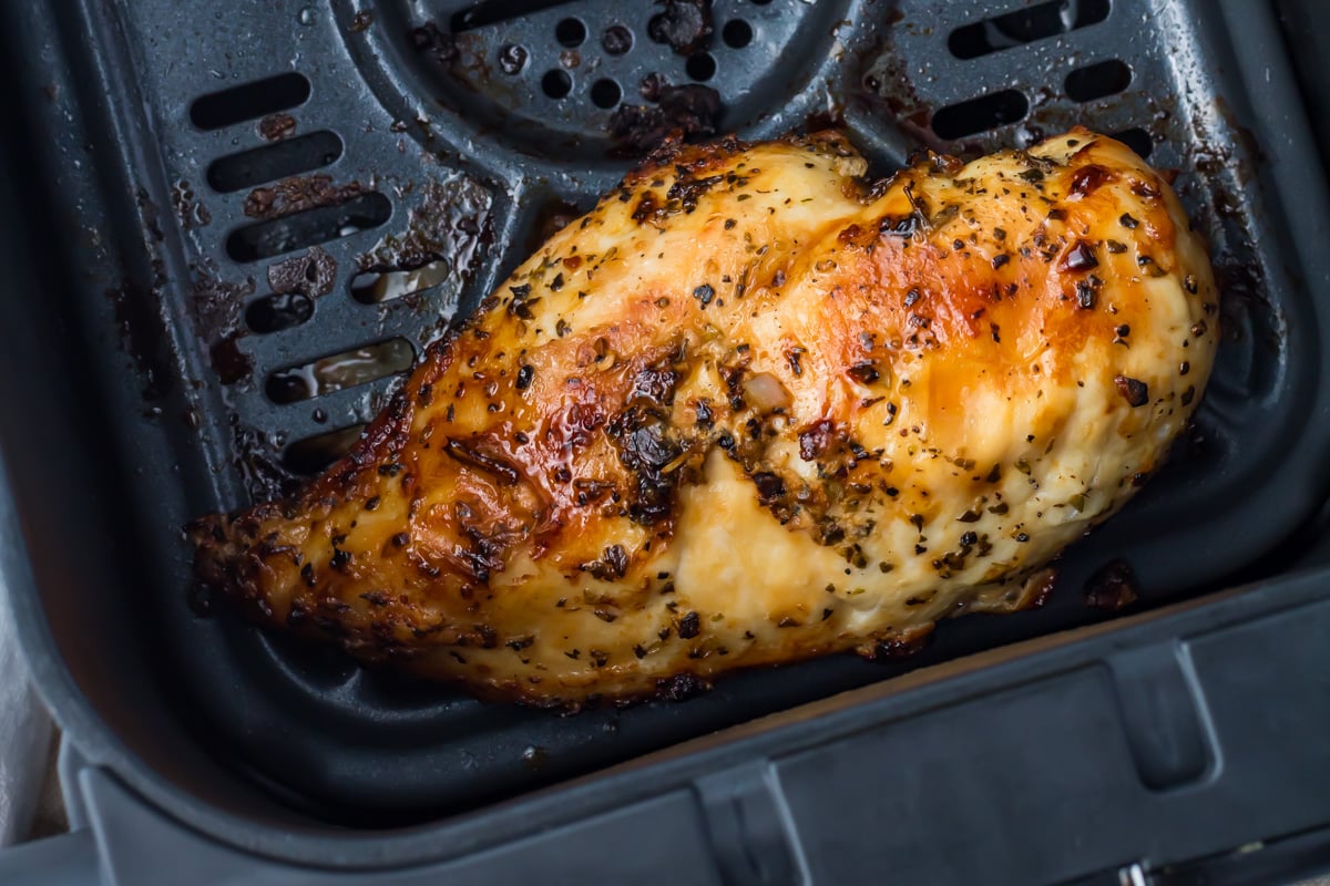 Cooked, seasoned chicken breast sits inside a ninja air fryer basket, showing a golden-brown, slightly crispy exterior with visible herbs and juices.