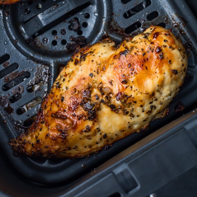 Cooked, seasoned chicken breast sits inside the basket of a ninja air fryer, showing a golden-brown, slightly crispy surface with visible herbs.