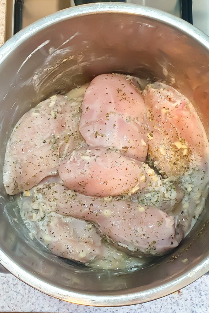 Raw seasoned chicken breasts marinating in a metal bowl, with visible herbs and chopped garlic&mdash;perfect for juicy air fryer chicken breasts in your Ninja.