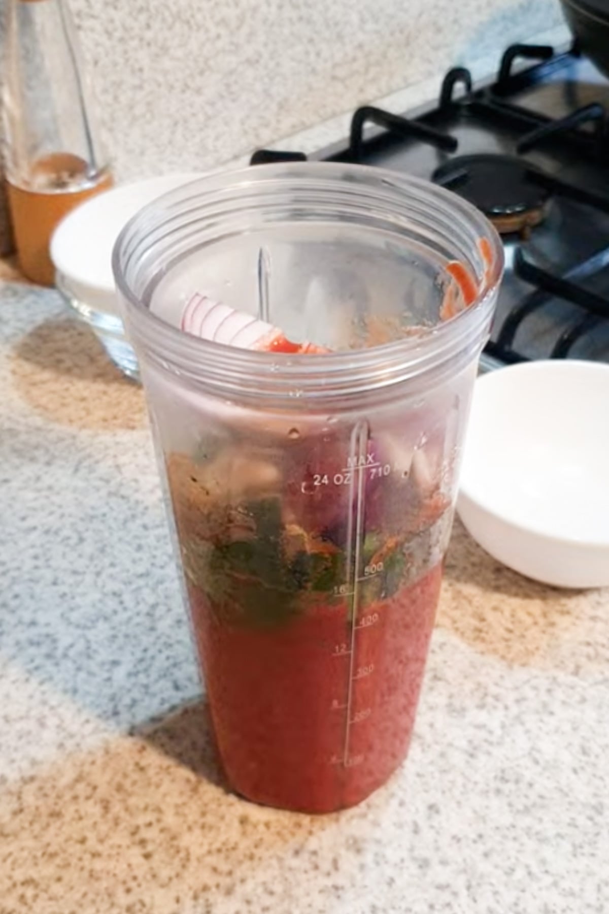 A blender cup on a kitchen counter filled with chopped vegetables and liquid, ready to be blended.