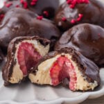 Frozen yogurt bites with a whole raspberry center, displayed on a plate. One piece is cut open to reveal the layers inside.