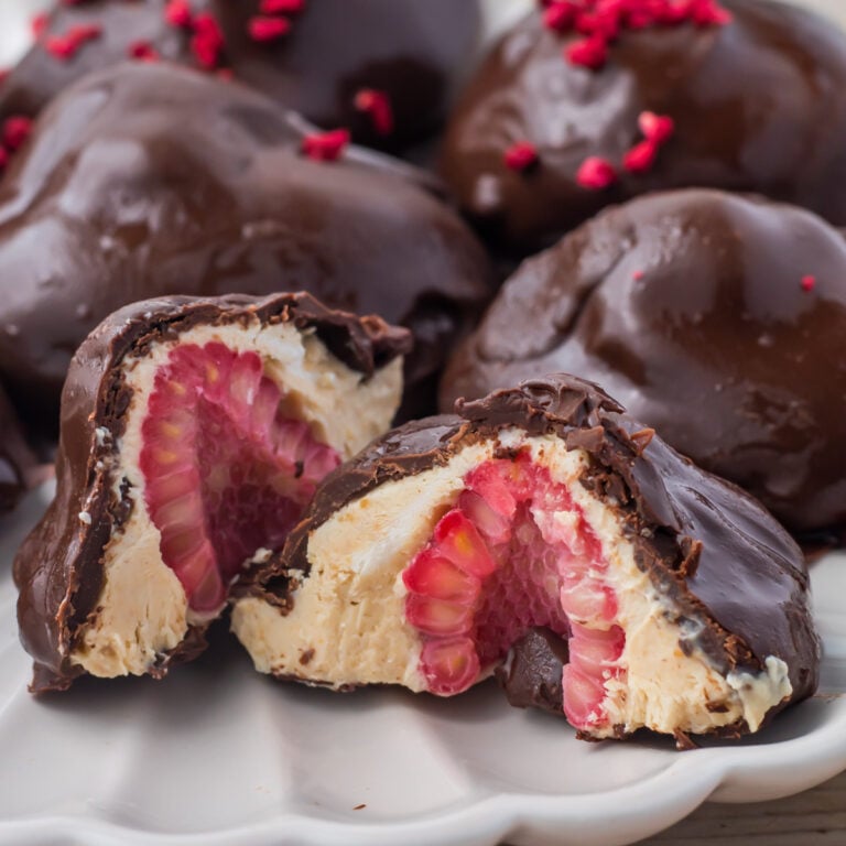 Frozen yogurt bites with a whole raspberry center, displayed on a plate. One piece is cut open to reveal the layers inside.