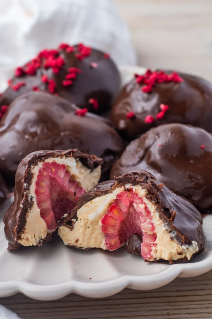 Frozen yogurt bites with raspberries arranged on a white plate with some pieces cut open to show the filling.