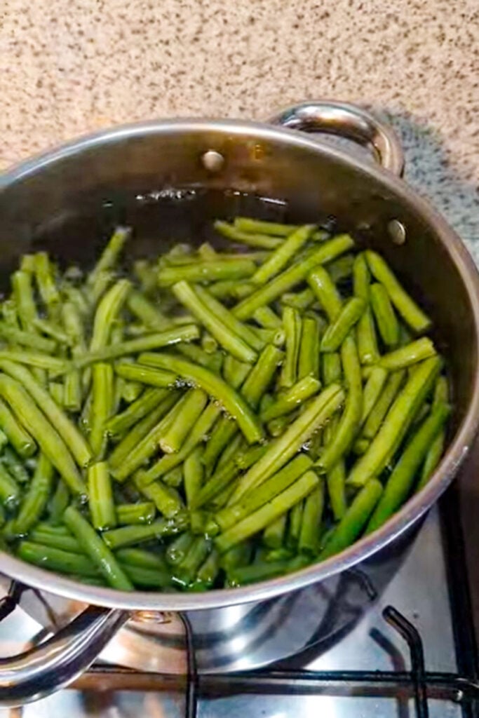 Honey Mustard Green Beans boiling in a stainless steel pot on a gas stove.