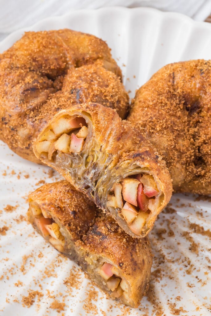 A sliced air fryer apple donut with a golden, flaky crust, filled with diced apples and sprinkled with brown sugar, displayed on a white plate.