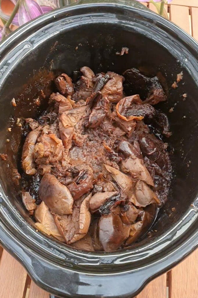 Sliced cooked apples in a black slow cooker, resting on a wooden table.