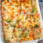cheesy chicken broccoli rice casserole with chicken, broccoli, and carrots covered in melted cheese in a white rectangular baking dish.