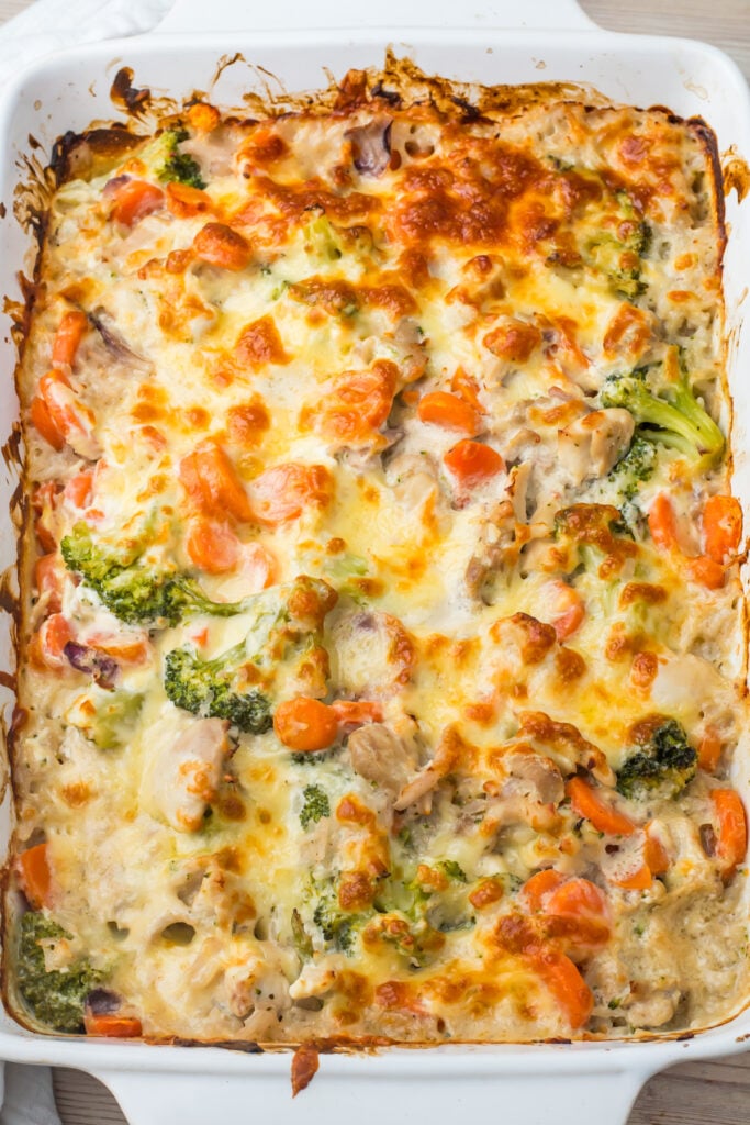 cheesy chicken broccoli rice casserole in a white dish containing broccoli, carrots, and chicken, topped with melted, browned cheese.