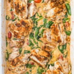an overhead photo of marry me chicken orzo bake: sliced seasoned chicken breasts served over a creamy orzo pasta bake with spinach and cherry tomatoes in a white baking dish.