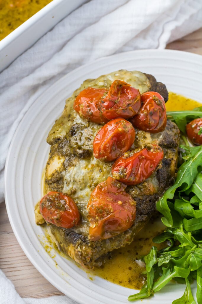 Pesto Chicken Bake topped with pesto, melted cheese, and roasted cherry tomatoes, served with a side of arugula.