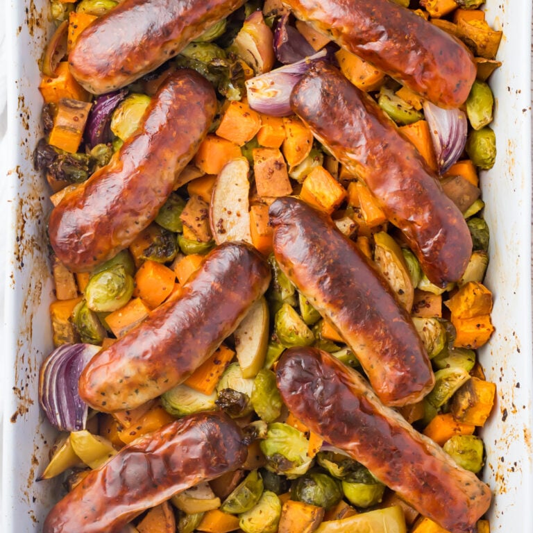 Sausage sweet potato bake in a baking dish with sweet potatoes, Brussels sprouts, apples, and red onion.