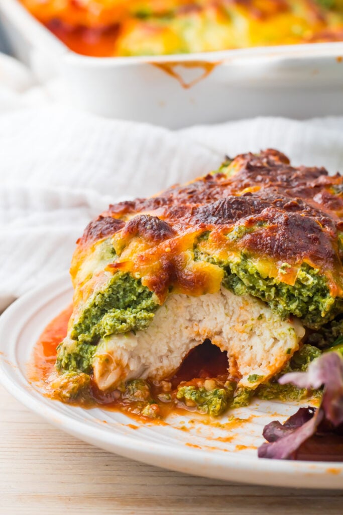 A baked spinach ricotta chicken breast topped with a layer of spinach, ricotta, and melted cheese, served in a tomato sauce.